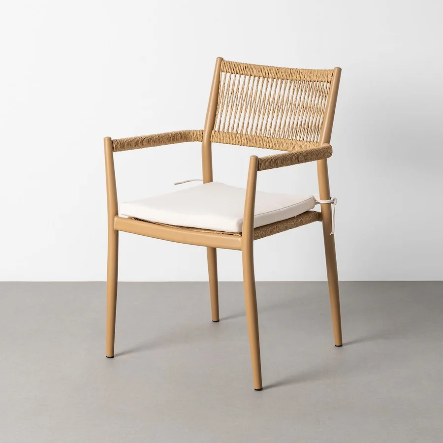 Chaise de jardin en rotin synthétique à dossier droit et accoudoirs, avec coussin d'assise clair, devant un mur blanc