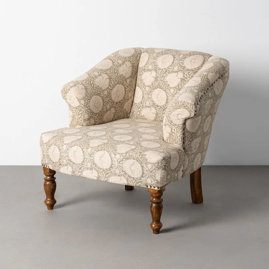 Fauteuil à fleurs en tissu beige à pieds tournés en bois, vu de trois quarts devant un mur clair