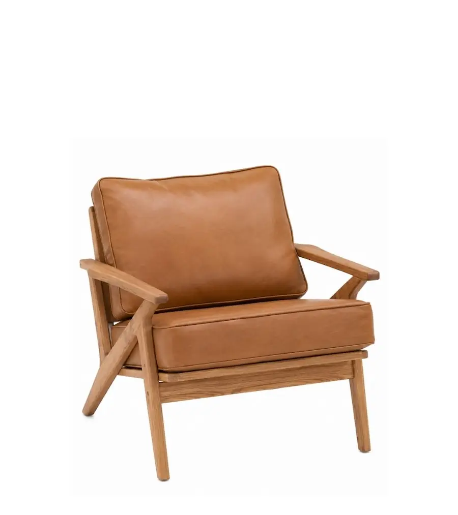 Fauteuil Adam en chêne et simili cuir camel, montants croisés et coussins à passepoil, vu de trois quarts