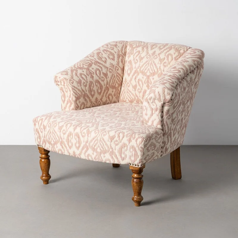 Fauteuil à imprimé rose et crème, pieds tournés en bois, vu de trois quarts devant un mur clair