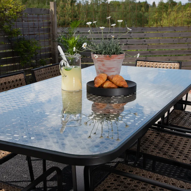 Table de jardin rectangulaire Paola en verre et tressage, vue de trois quarts sur pieds noirs