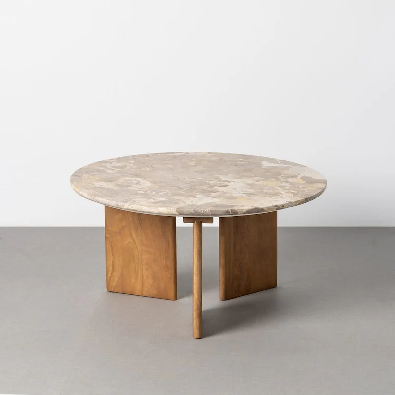 Table basse ronde en pierre beige veinée sur trois pieds en bois, vue de face sur fond gris