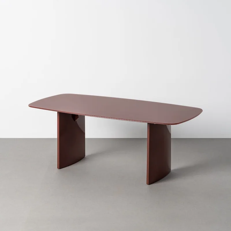 Table basse bordeaux Ixia, plateau en verre aux angles arrondis sur deux larges pieds, vue de trois quarts