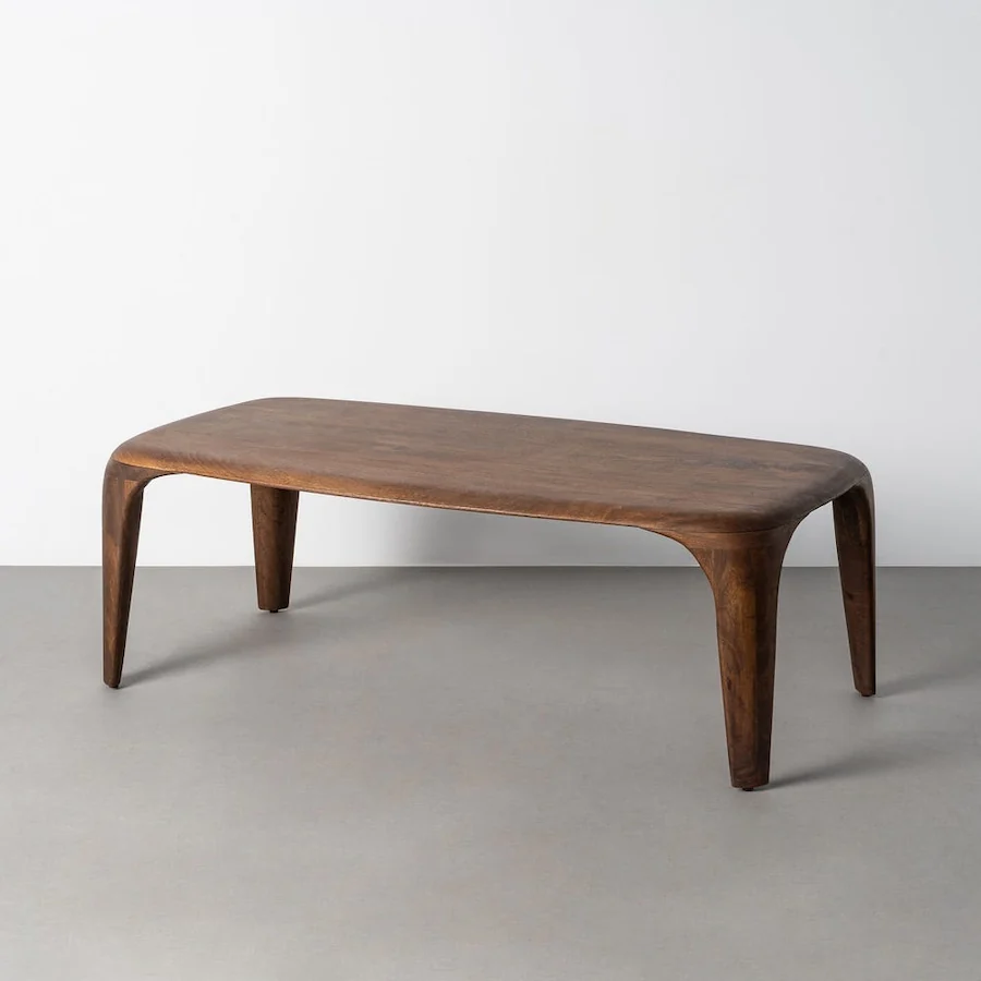Table basse en bois de manguier Ixia, plateau brun foncé aux angles arrondis et pieds galbés, sur sol gris